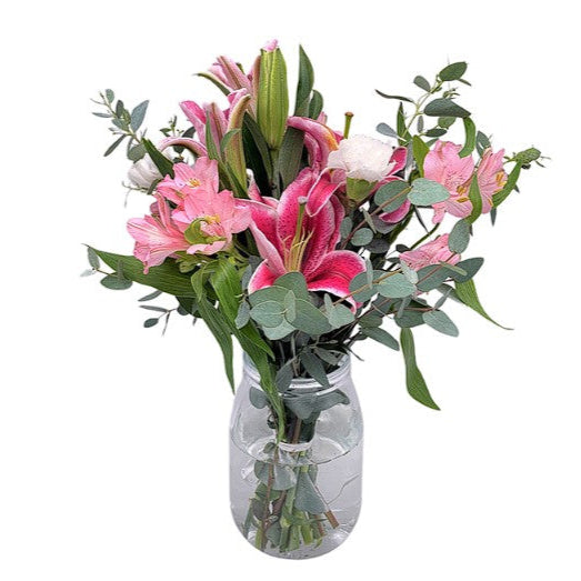 Bouquet of pink lilies and greenery in a clear vase on a white background